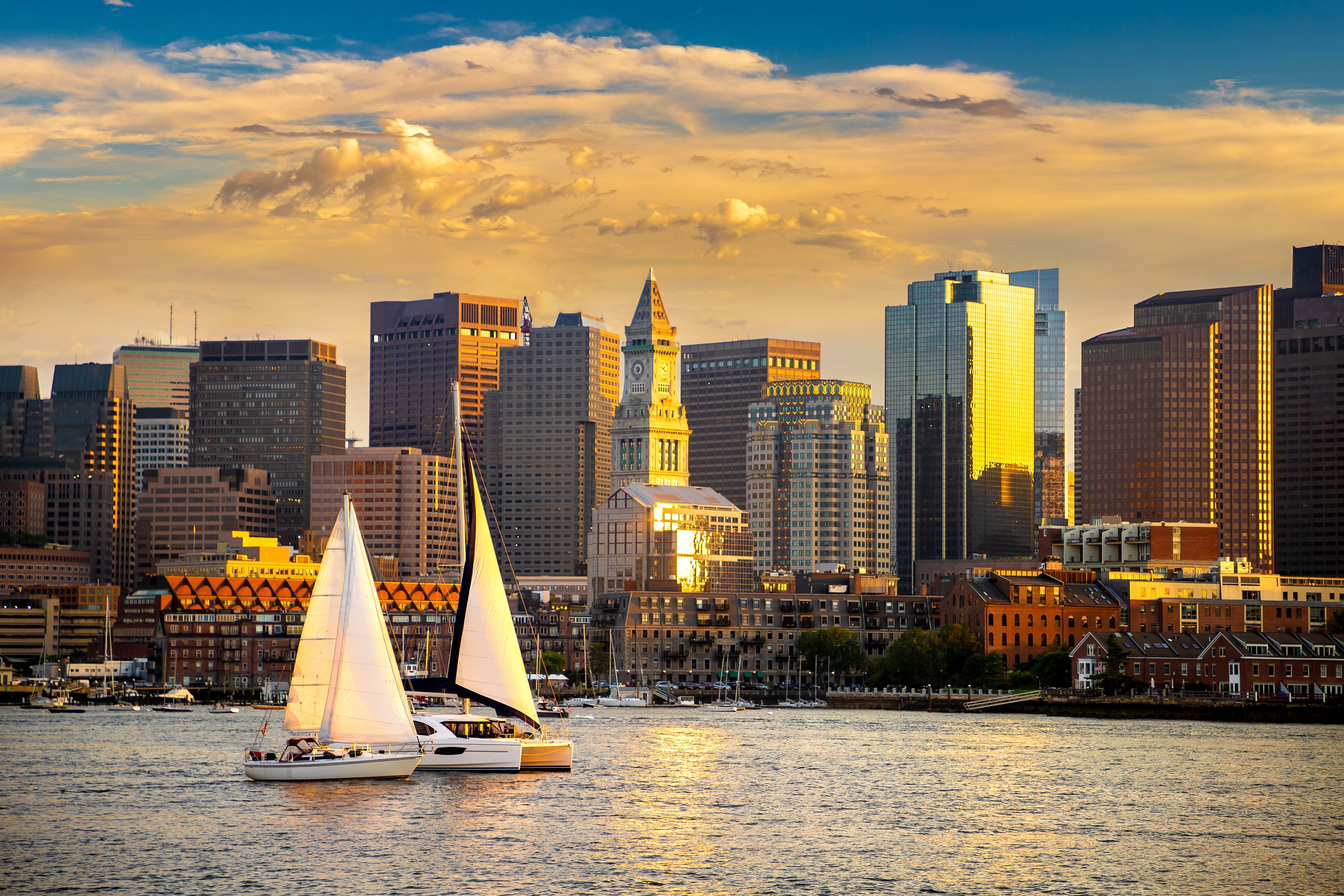 Sail boats in habror with Bostom skyline behind at sunset
